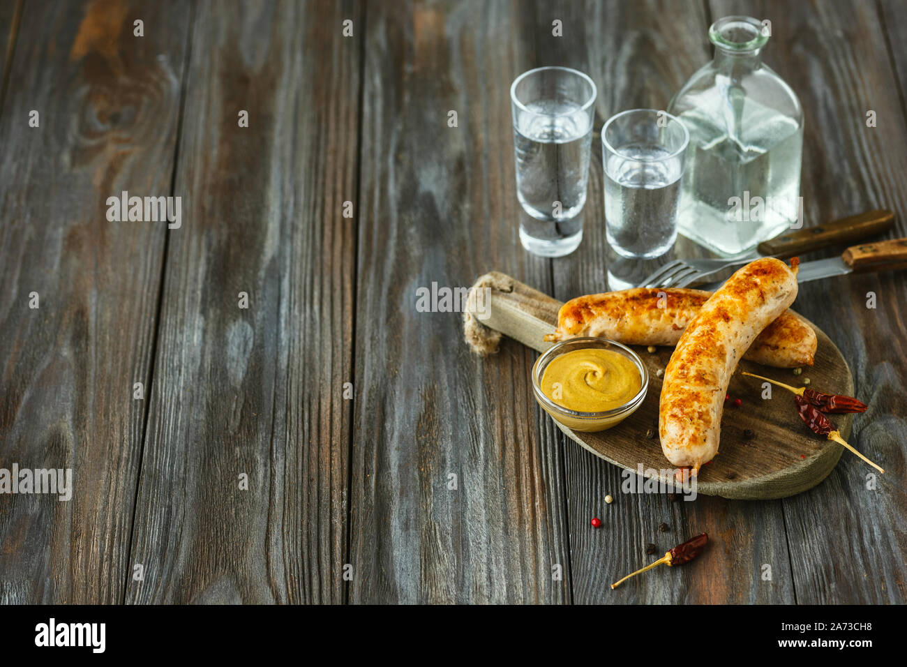 Vodka con salsicce fritte e salsa su sfondo di legno. Alcol puro artigianato drink e snack tradizionali. Lo spazio negativo. Celebrando e cibo delizioso. Foto Stock