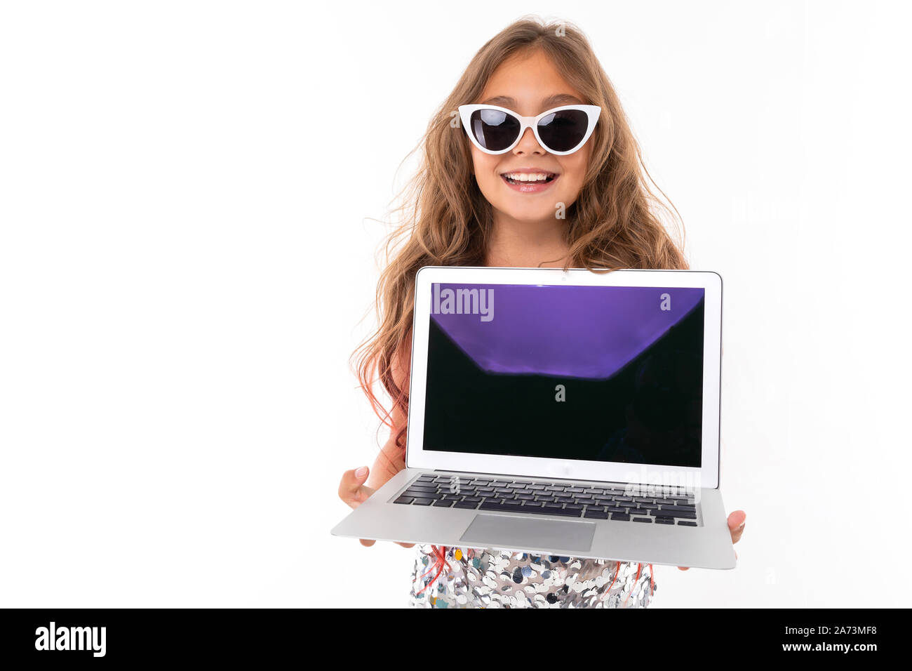 Schoolgirl in occhiali da sole può contenere un computer portatile nelle sue braccia al livello del petto, con un largo sorriso con denti guarda la telecamera Foto Stock