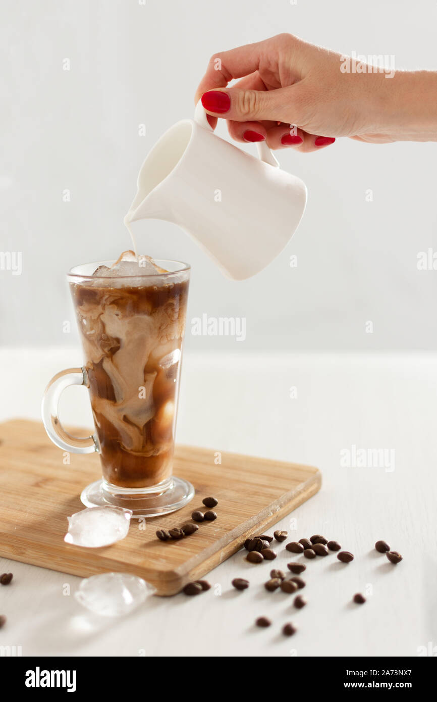 Caffè ghiacciato in un bicchiere con panna versato sopra. Caffè freddo con cubetti di ghiaccio e crema. Foto Stock