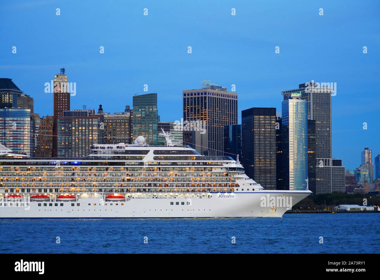 Oceania Cruises Riviera nave da crociera passando inferiore dello skyline di Manhattan nel porto di New York al crepuscolo. Foto Stock