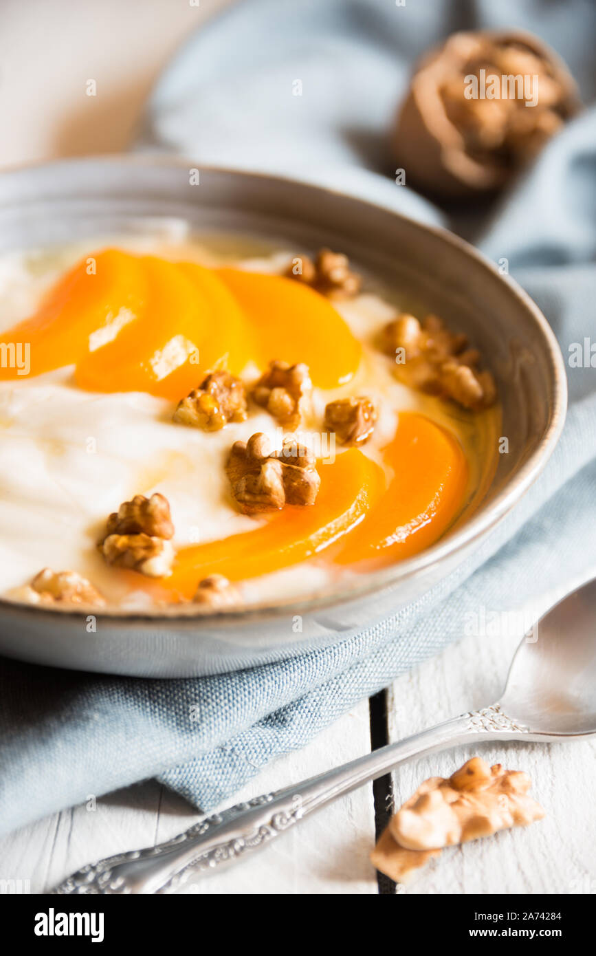 Yogurt con pesche, noci e miele in una ciotola blu Foto Stock