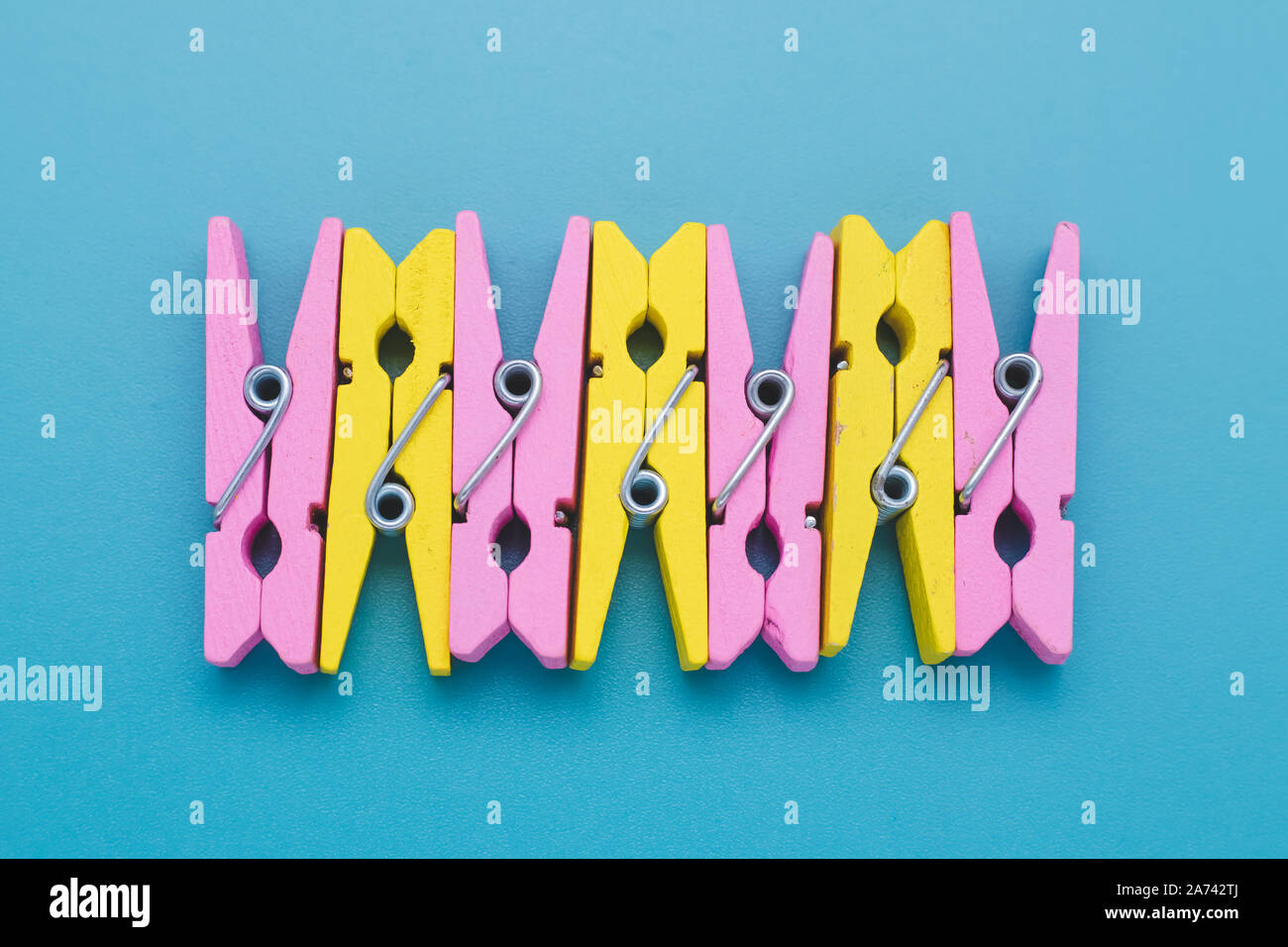 Concetto di divertimento dell'umore. In legno colorato clothespins su carta blu sullo sfondo. Creative design minimale. Giallo e rosa clothespin, abstract multicolor Foto Stock