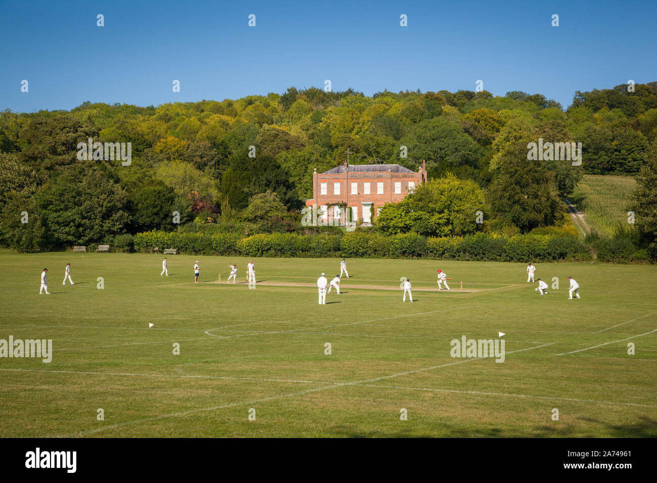 Una partita di cricket a Hambleden, Buckinghamshire, con la casa Kenricks classificata Grade II alle spalle, costruita nel 1725 Foto Stock