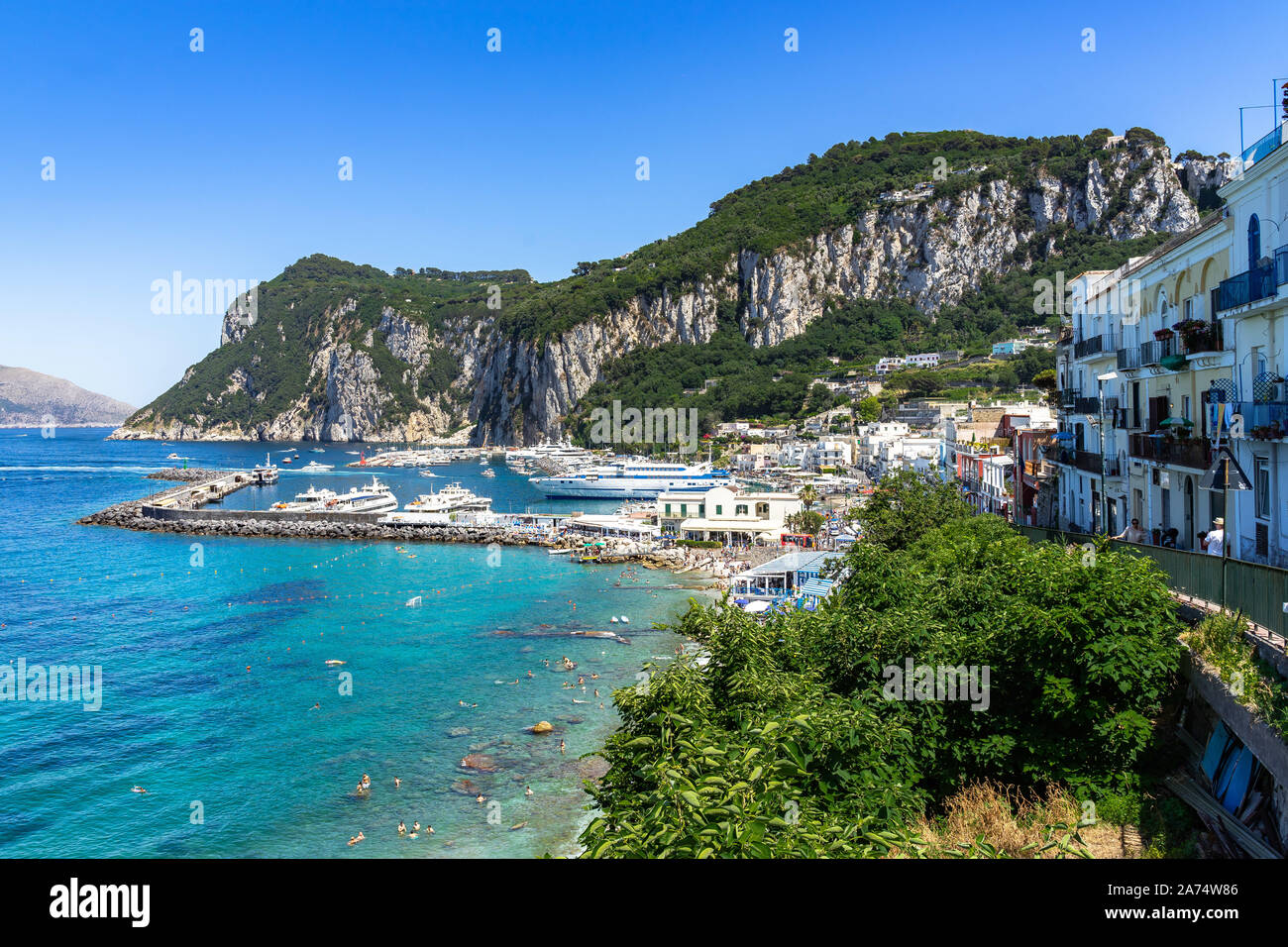 Bellissima vista di Marina Grande porto di Capri lambite da acque turchesi con la Punta del Capo in background, Italia Foto Stock