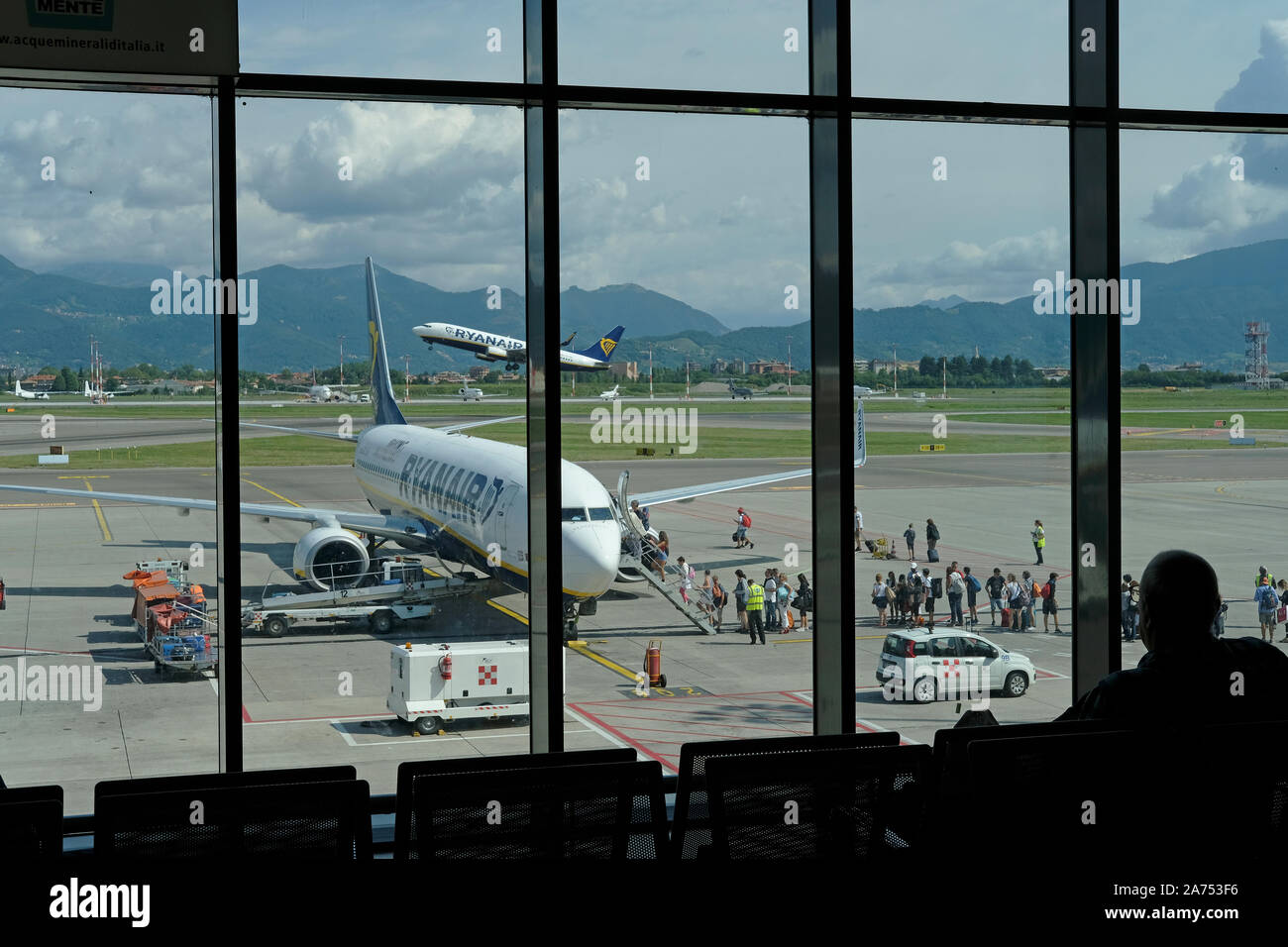 I passeggeri di salire a bordo di un aereo Ryanair mentre un altro aereo decolla Foto Stock