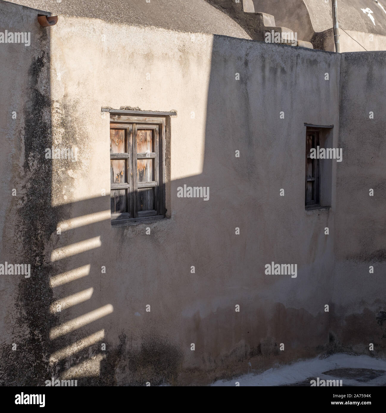 Linee di ombra delle strisce di stecche di sole splendente su una vecchia casa di abitazione home parete esterna Santorini Foto Stock