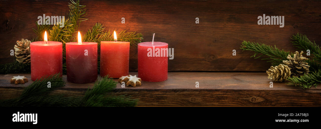 Terzo Avvento, tre delle quattro candele rosse sono illuminati con una fiamma, Abete rami e decorazione di Natale in scuro legno rustico, ampio formato panoramico con co Foto Stock