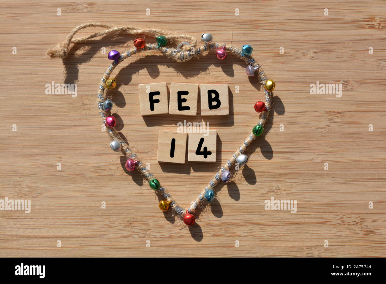 Feb 14, parole in 3d alfabeto di legno lettere a forma di cuore, telaio con campane colorati su un legno di bambù sfondo. Concetto creativo, il giorno di San Valentino Foto Stock