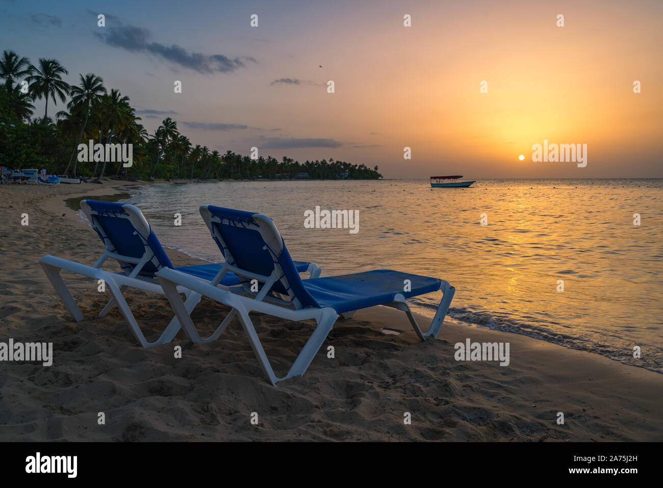 Due sedie a sdraio e barca sfondo sulla spiaggia tropicale al tramonto,Repubblica Dominicana,Bahia Principe spiaggia. Foto Stock