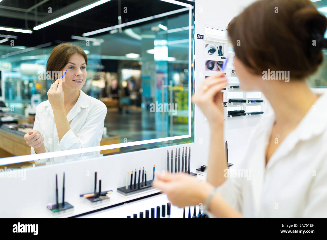 Ritratto di giovane donna in un negozio di cosmetici è messa sul make-up con blue eye-matita nella parte anteriore dello specchio. Foto con la profondità di campo Foto Stock