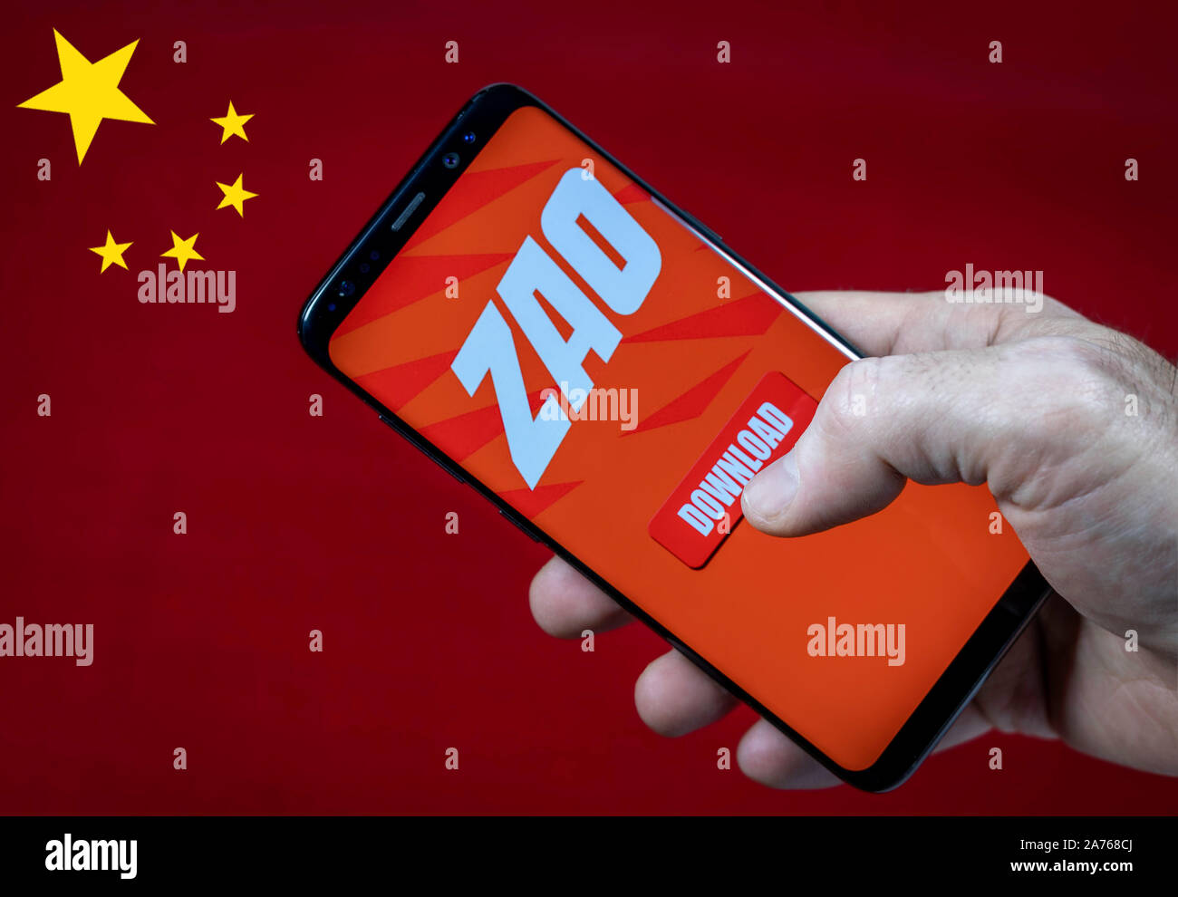 Maschio di mano azienda smartfone con ZAO app logo e il pulsante di download contro bandiera della Cina. Foto Stock