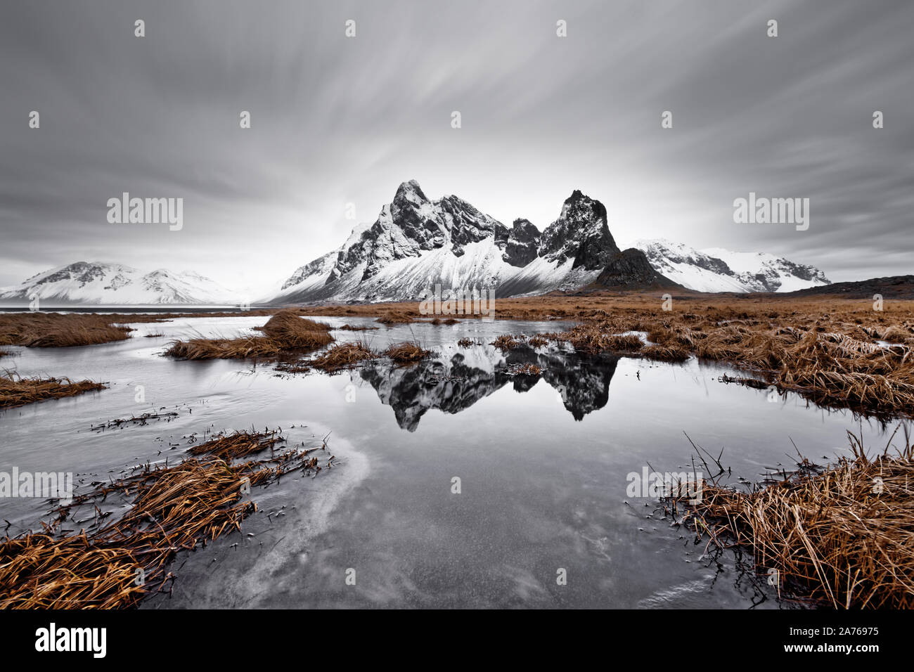 Coperto di neve e la formazione di montagna è riflessa in uno stagno, ciuffi di erba in e intorno allo stagno, lame di erba sono parzialmente spostata dal vento Foto Stock