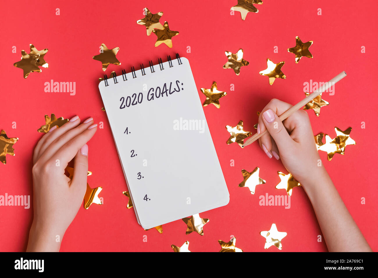 Donna di mani tenendo una matita vicino al blocco note con il testo 2020 Obiettivi sul con uno sfondo rosso a forma di stella coriandoli. Foto Stock
