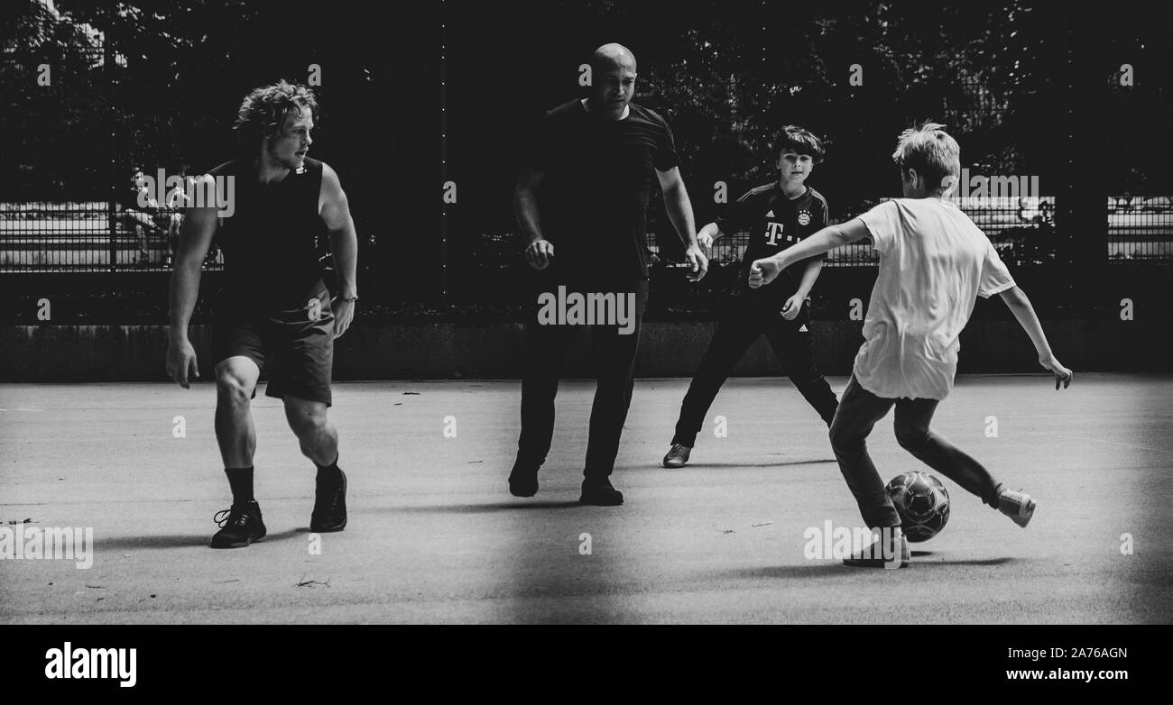 I bambini Giocare calcio di strada con adulti Foto Stock