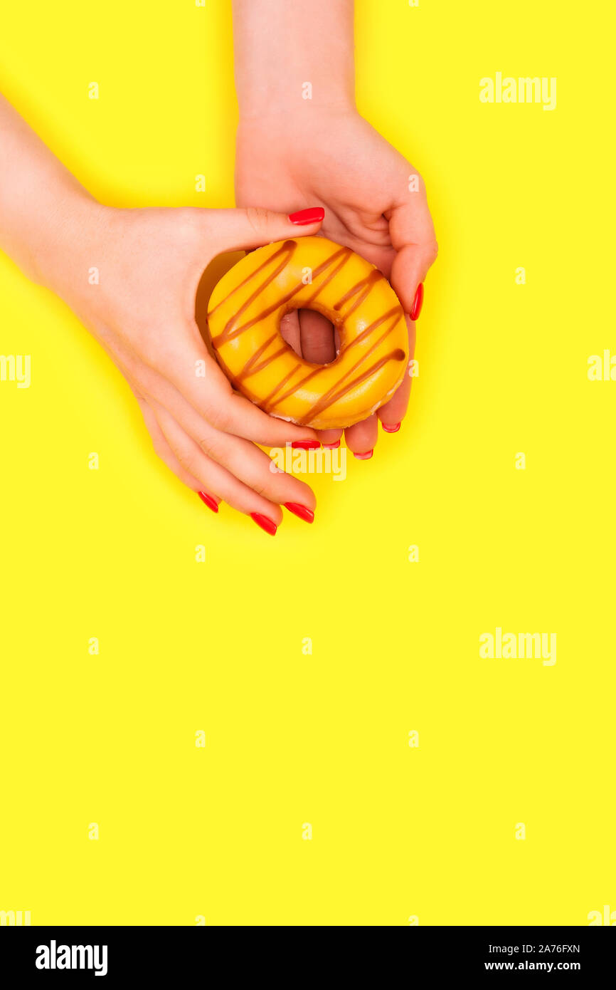 Alla moda ed elegante femmina rosso manicure. Le mani di una donna bella detiene un dolce ciambella di giallo. Sfondo giallo. Foto Stock