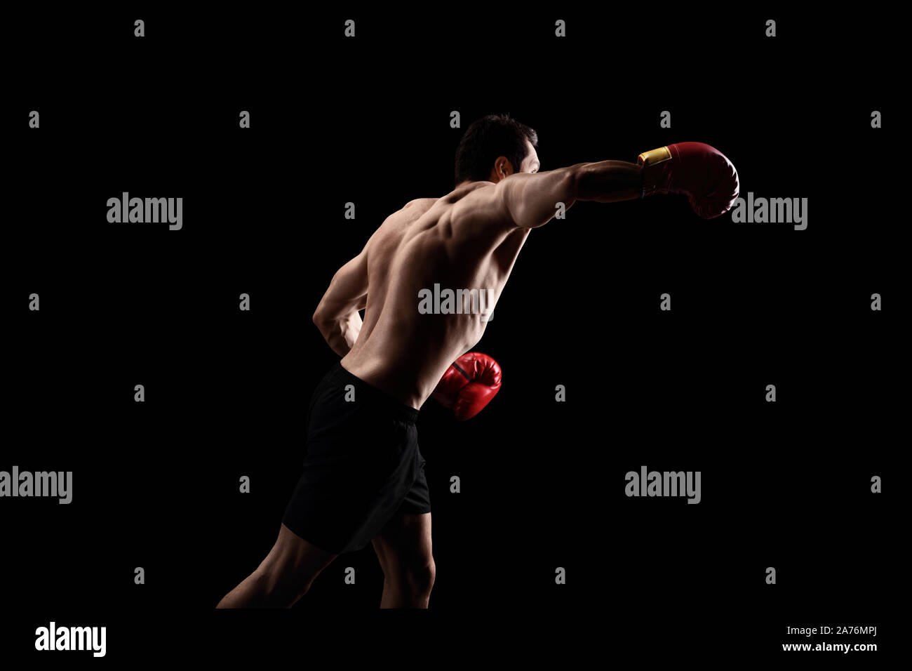 Forte uomo muscolare allenamento con i guantoni su uno sfondo nero Foto Stock