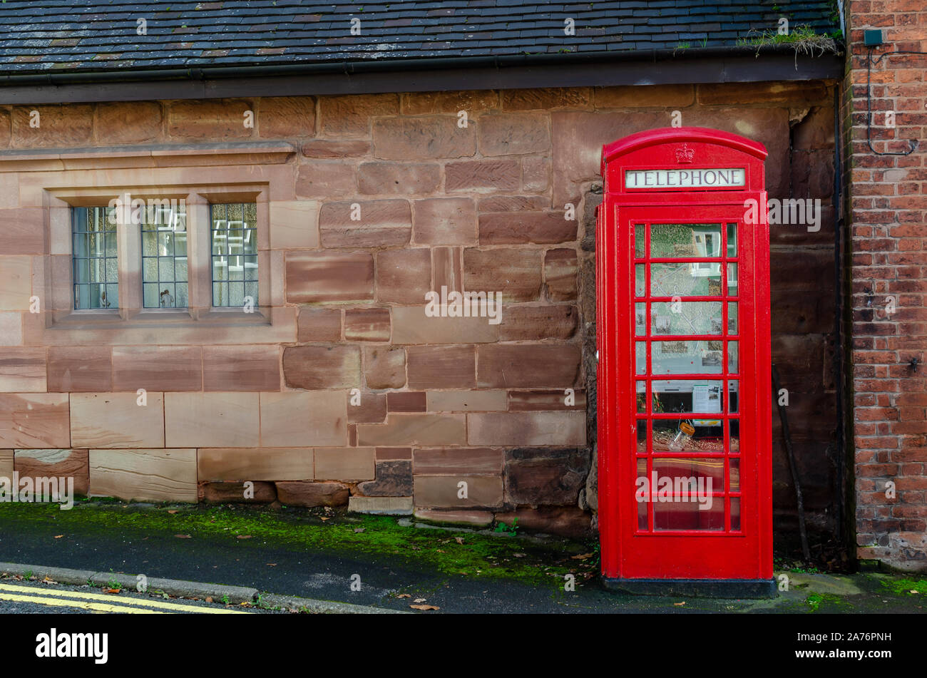 Iconico telefono rosso accanto a un vecchio muro di pietra visto ad Oulton, Staffordshire, Regno Unito. Foto Stock
