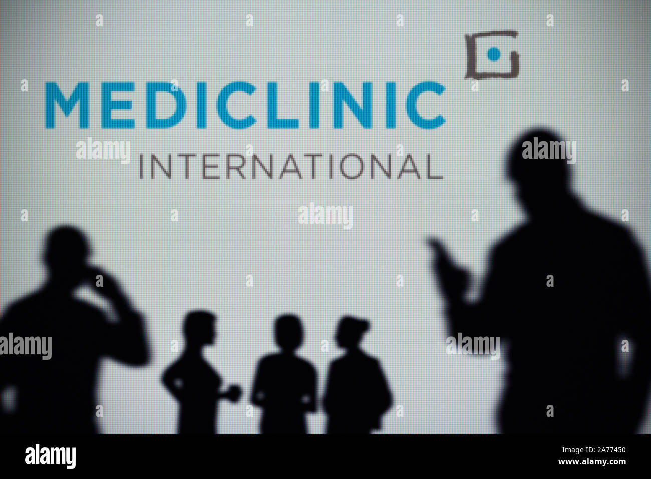 Il Mediclinic International logo è visibile su uno schermo a LED in background mentre si profila una persona utilizza uno smartphone (solo uso editoriale) Foto Stock