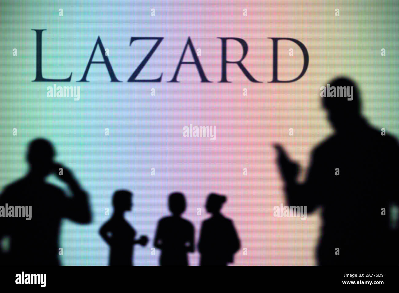 La Lazard asset management company logo è visibile su uno schermo a LED in background mentre si profila una persona utilizza uno smartphone (solo uso editoriale) Foto Stock