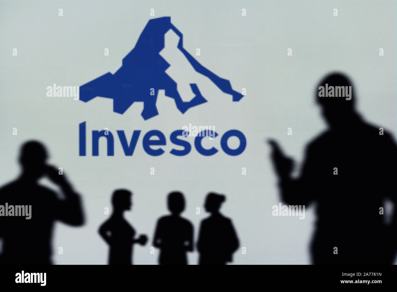 L'Invesco logo è visibile su uno schermo a LED in background mentre si profila una persona utilizza uno smartphone (solo uso editoriale) Foto Stock