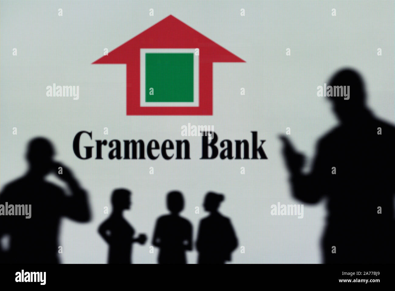 La Grameen Bank logo è visibile su uno schermo a LED in background mentre si profila una persona utilizza uno smartphone (solo uso editoriale) Foto Stock