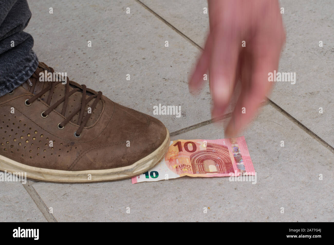 Qualcuno ha trovato 10 euro sulla strada, fissandolo con il suo piede, il tentativo di afferrare la banconota. La mano è fuori fuoco per il movimento e la dinamica. Foto Stock