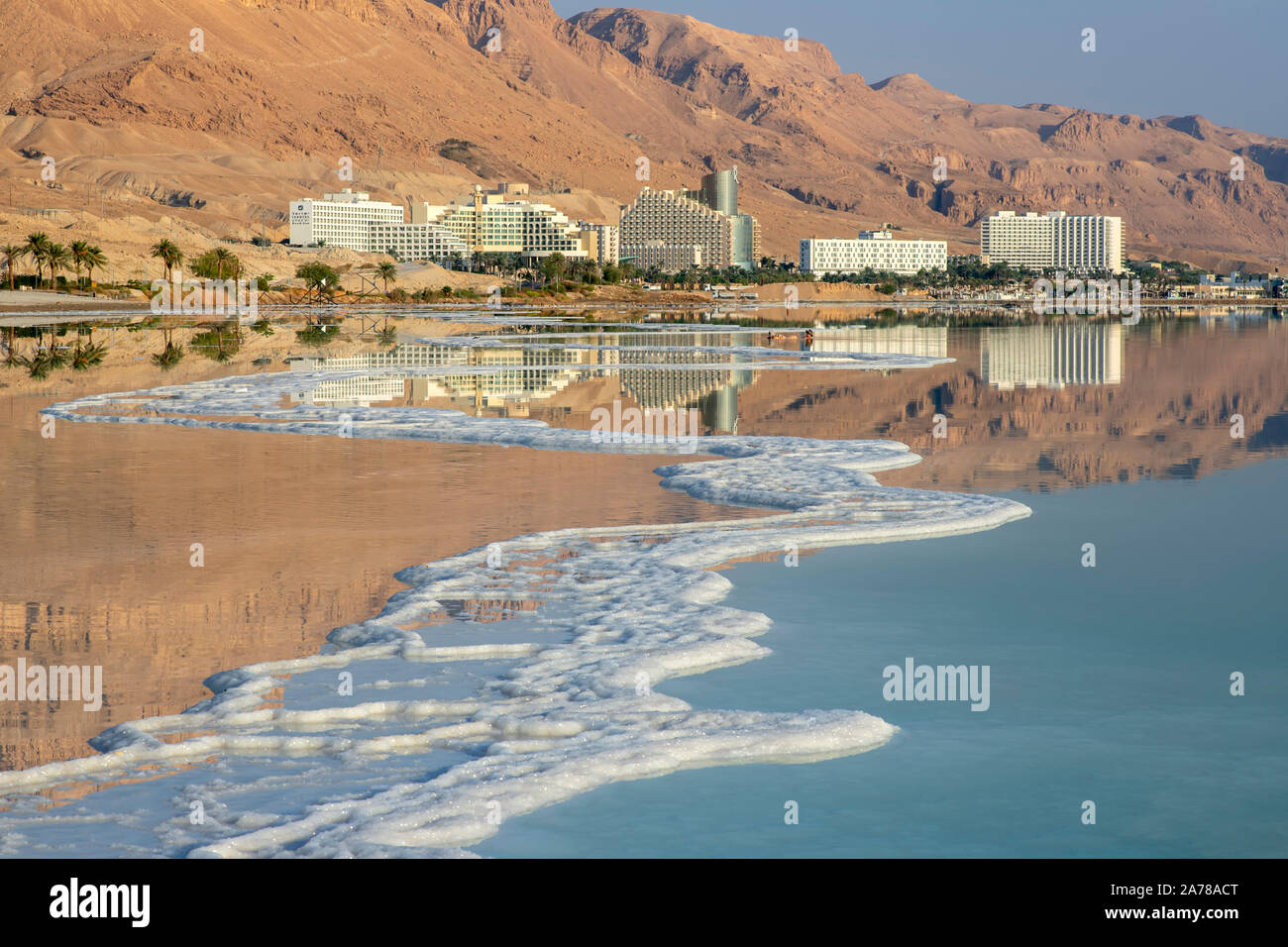 La riflessione di montagne, di alberghi e di palme in acqua del Mar Morto con formazioni di sale. Israele Foto Stock