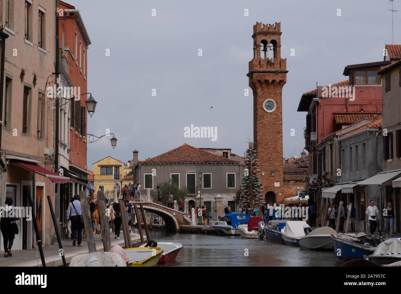 Central Canal Grande di Murano, Venezia riempito con barche a motore e i turisti intorno al vetro molte botteghe correlate su un luminoso giorno con torre e ponte. Foto Stock