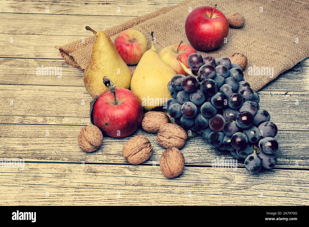 Deliziosa Autumn harvest - su tela, un sfondo di legno pieno di pere mature, mele, uva e noci Foto Stock
