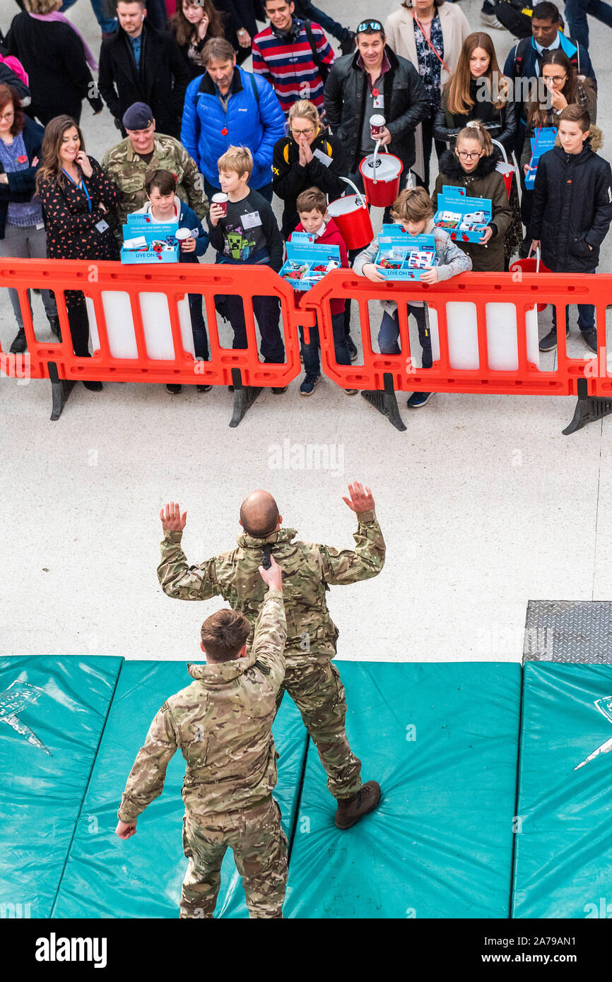 Famiglia di volontariato collezionisti guardare il display del combattimento disarmati dai Royal Marines, a Waterloo Station - 2000 personale di servizio di unire le forze con i veterani, volontari e celebrità nel tentativo di sollevare £ 1 m in un unico giorno per il Royal British Legion durante la London Poppy Day. Credito: Guy Bell/Alamy Live News Foto Stock