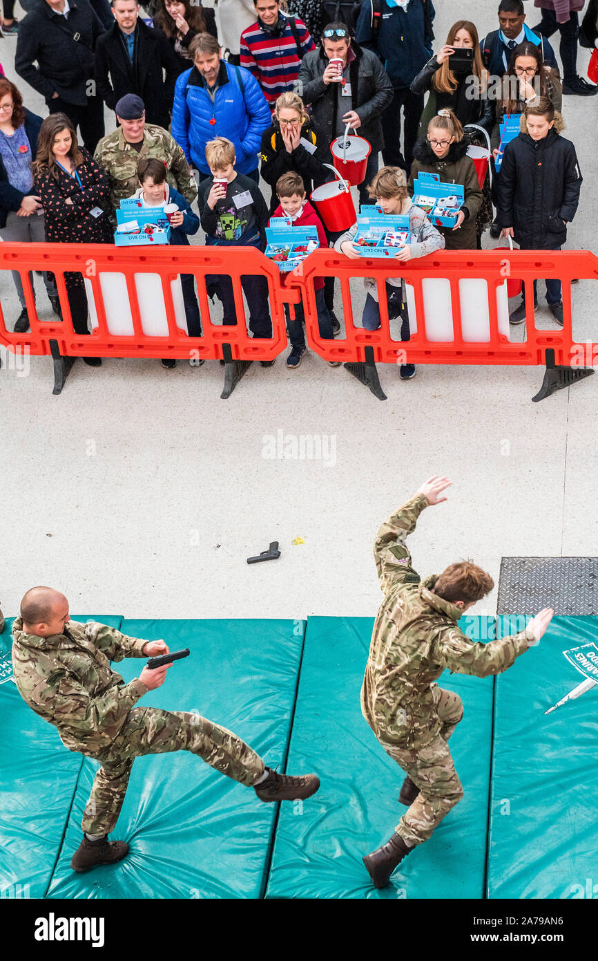 Famiglia di volontariato collezionisti guardare il display del combattimento disarmati dai Royal Marines, a Waterloo Station - 2000 personale di servizio di unire le forze con i veterani, volontari e celebrità nel tentativo di sollevare £ 1 m in un unico giorno per il Royal British Legion durante la London Poppy Day. Credito: Guy Bell/Alamy Live News Foto Stock