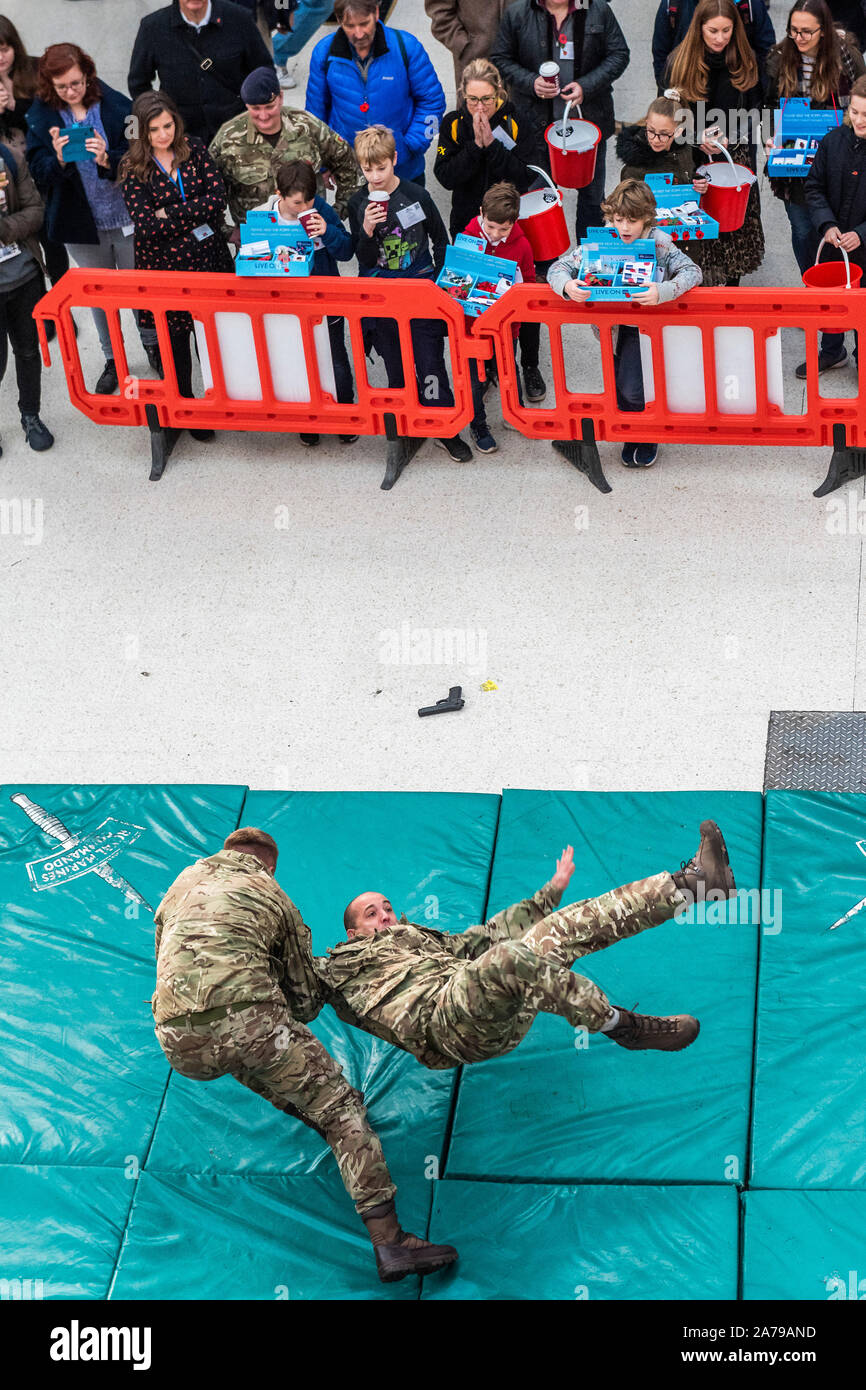 Famiglia di volontariato collezionisti guardare il display del combattimento disarmati dai Royal Marines, a Waterloo Station - 2000 personale di servizio di unire le forze con i veterani, volontari e celebrità nel tentativo di sollevare £ 1 m in un unico giorno per il Royal British Legion durante la London Poppy Day. Credito: Guy Bell/Alamy Live News Foto Stock