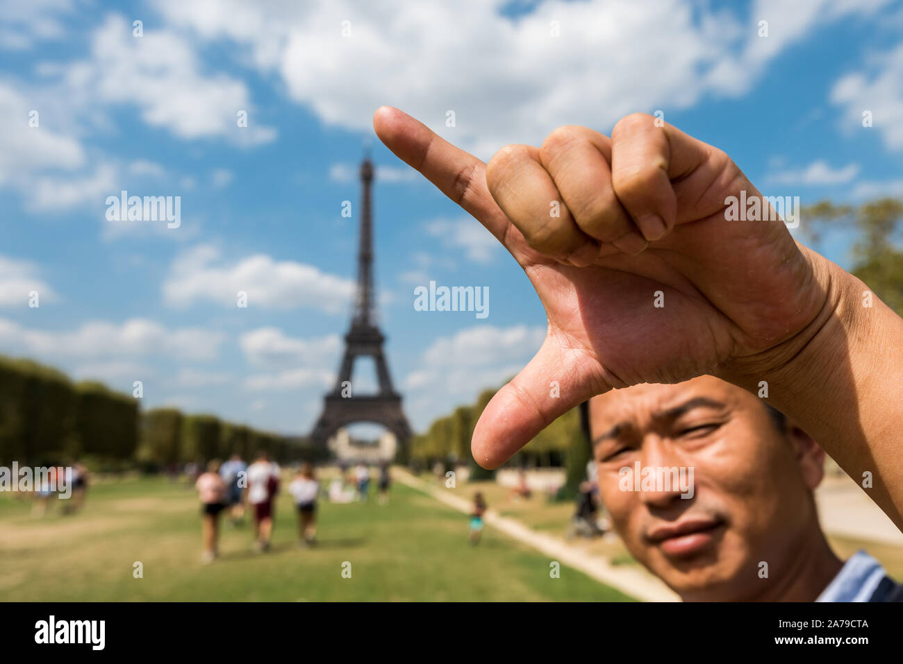 Un uomo Chinee utilizzando la sua mano per misurare la lunghezza della Torre Eiffel, un ferro battuto torre tralicciata su Champ de Mars a Parigi, Francia, chiamato dopo l'en Foto Stock