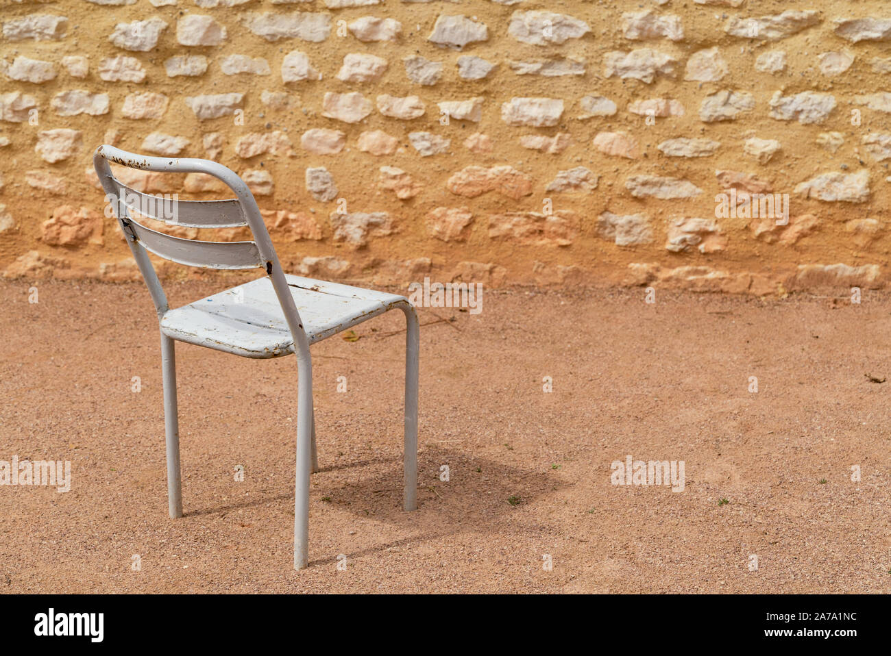 Un vuoto di metallo bianco sedia in un cortile di sabbia con una parete di roccia Foto Stock