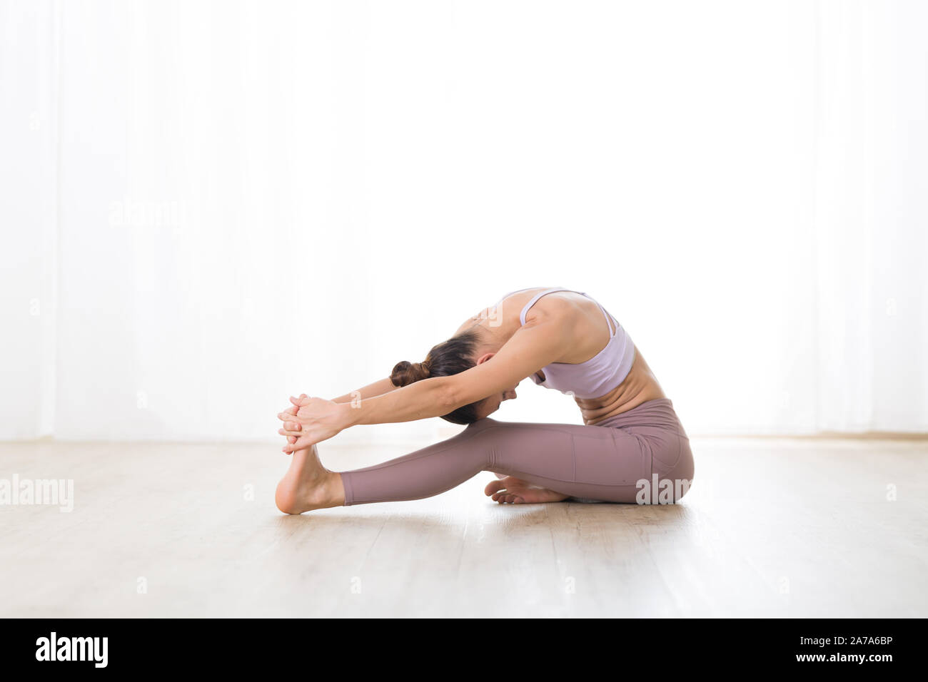 Ritratto di splendida sportiva attiva giovane donna a praticare yoga in studio. Bella ragazza pratica Janushiransa con Paschimotthanasana, testa a ginocchio Foto Stock