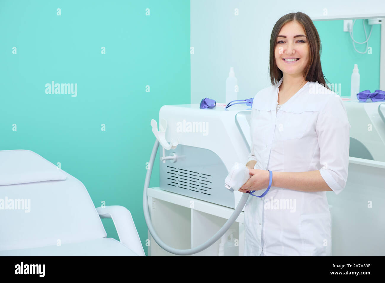 Sorridente medico in camice bianco in un salone di bellezza di depilazione laser e guardando la telecamera, copyspace Foto Stock