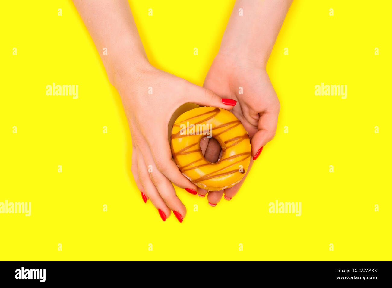 Alla moda ed elegante femmina rosso manicure. Le mani di una donna bella detiene un dolce ciambella di giallo. Sfondo giallo. Lay piatto. Foto Stock