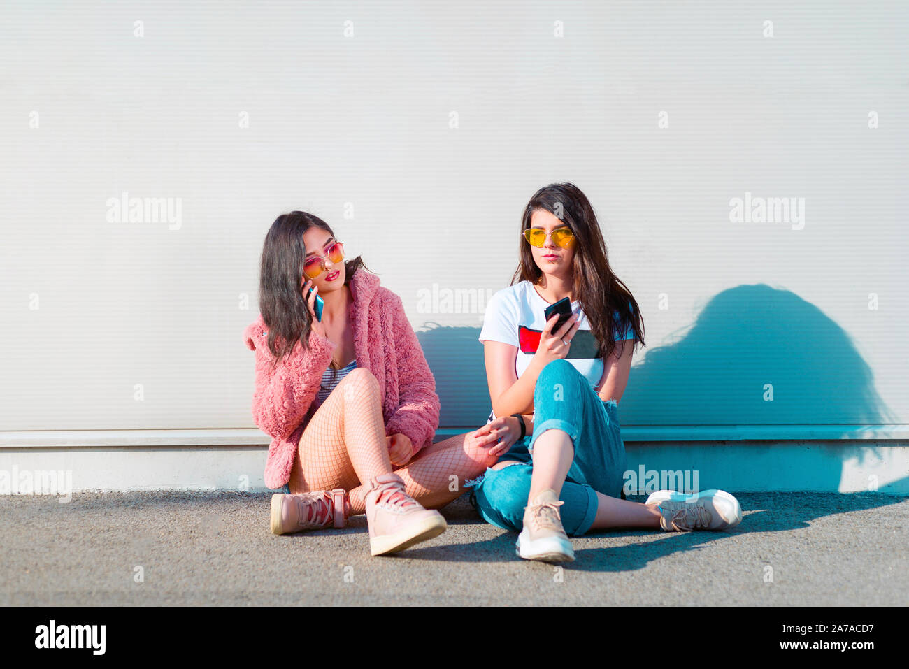 Due eleganti giovani donne utilizzando i telefoni cellulari Foto Stock