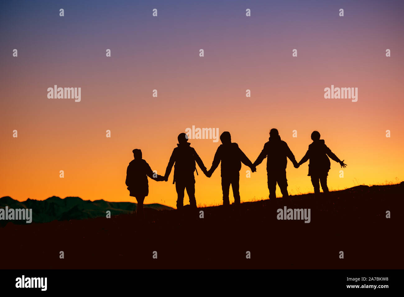 Sagome di gruppo di amici sono in piedi insieme al tramonto tempo contro la montagna Foto Stock