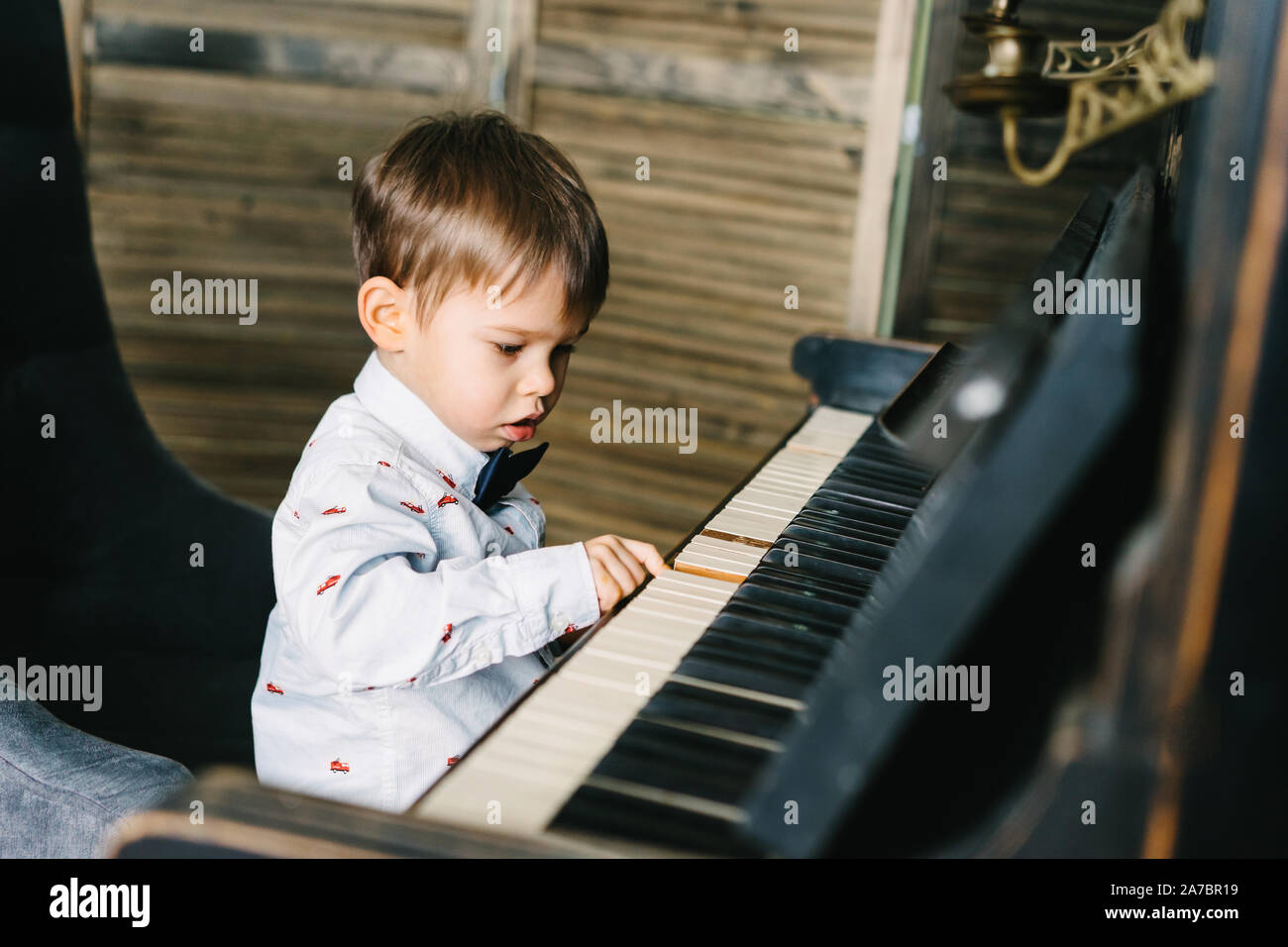 Un ragazzino in una smart shirt e bow tie siede a un grande pianoforte di sintonizzazione Foto Stock