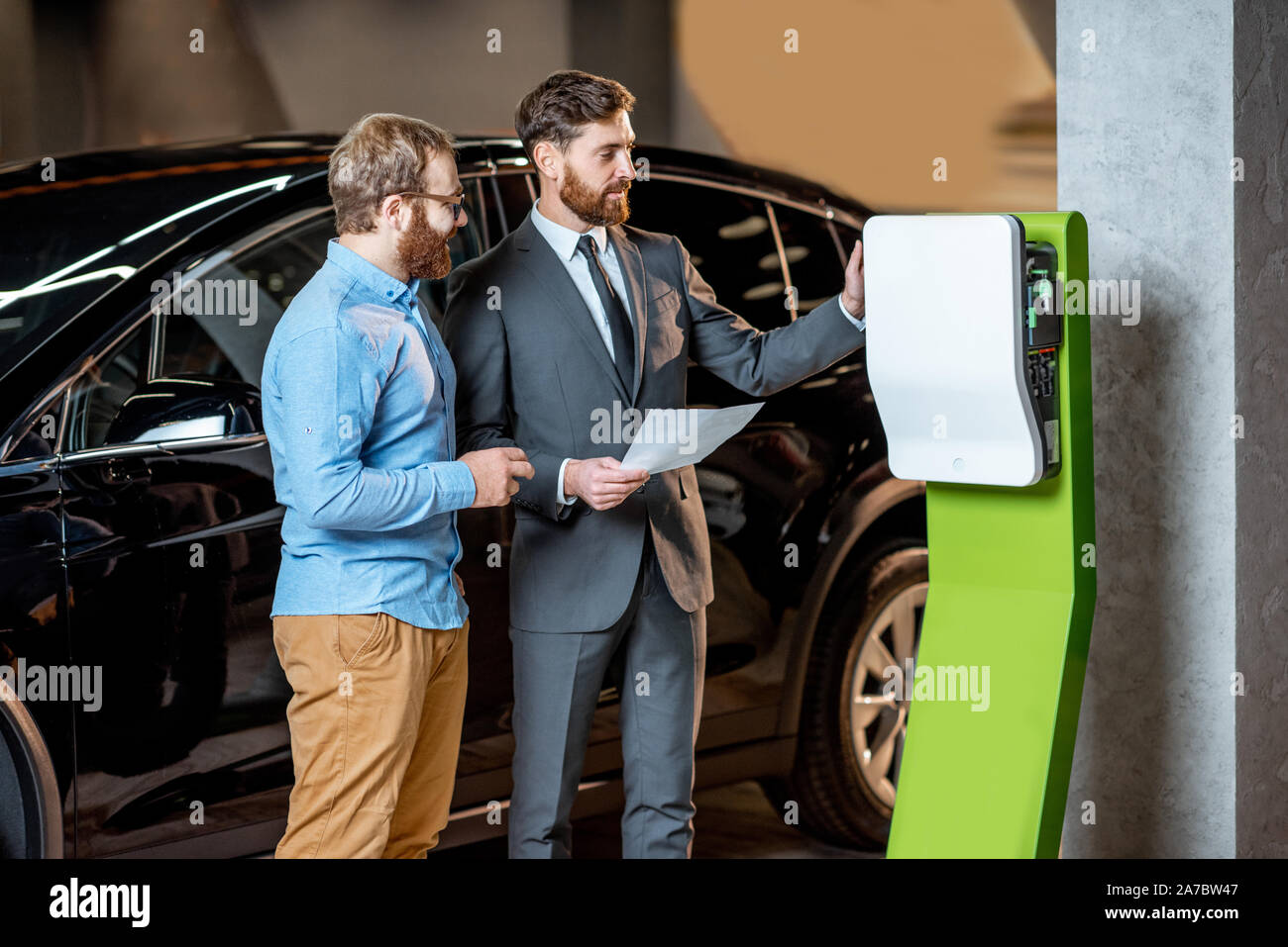 Il cliente con un consulente di vendita la scelta di una stazione di carica per un auto elettrica in corrispondenza di una concessionaria auto Foto Stock