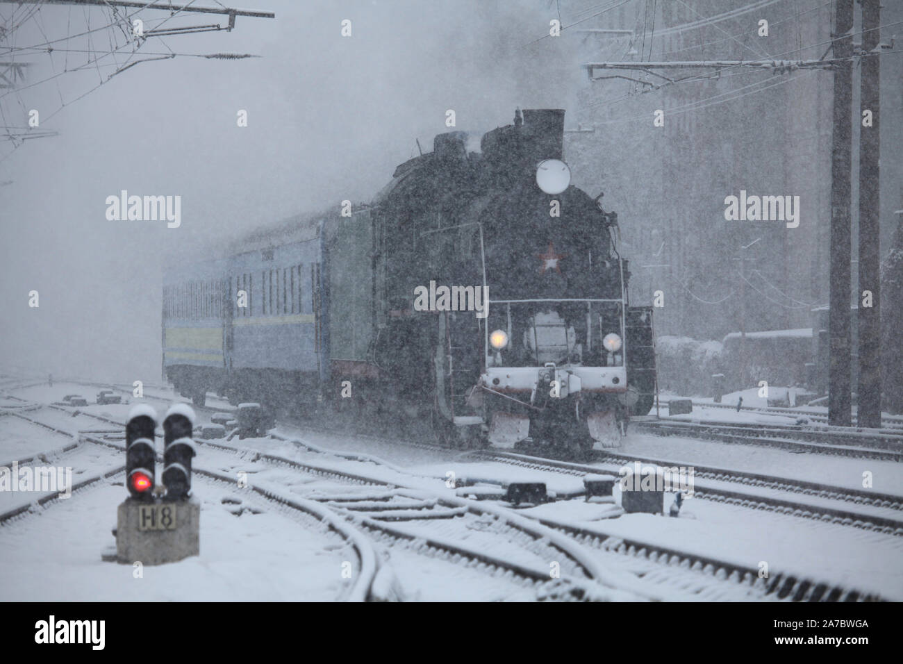 Anno nuovo ferroviario di neve durante una bufera di neve. Locomotiva (puffer) su sfocato sfondo innevato è arrivare alla stazione. Vacanza invernale, viaggi ferroviari Foto Stock