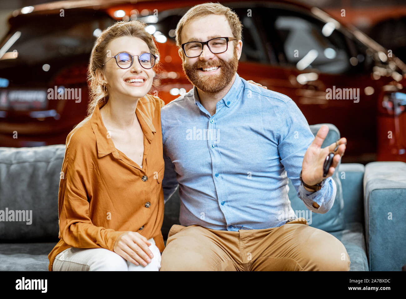 Ritratto di una giovane e felice coppia seduti insieme sul comodo divano e acquisto di una nuova auto presso la concessionaria Foto Stock