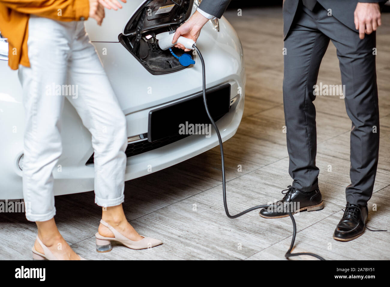 Sales Manager che mostra come caricare auto elettriche per un giovane client, collegando il filo nella presa auto presso la concessionaria auto. Vista ravvicinata con nessun volto Foto Stock
