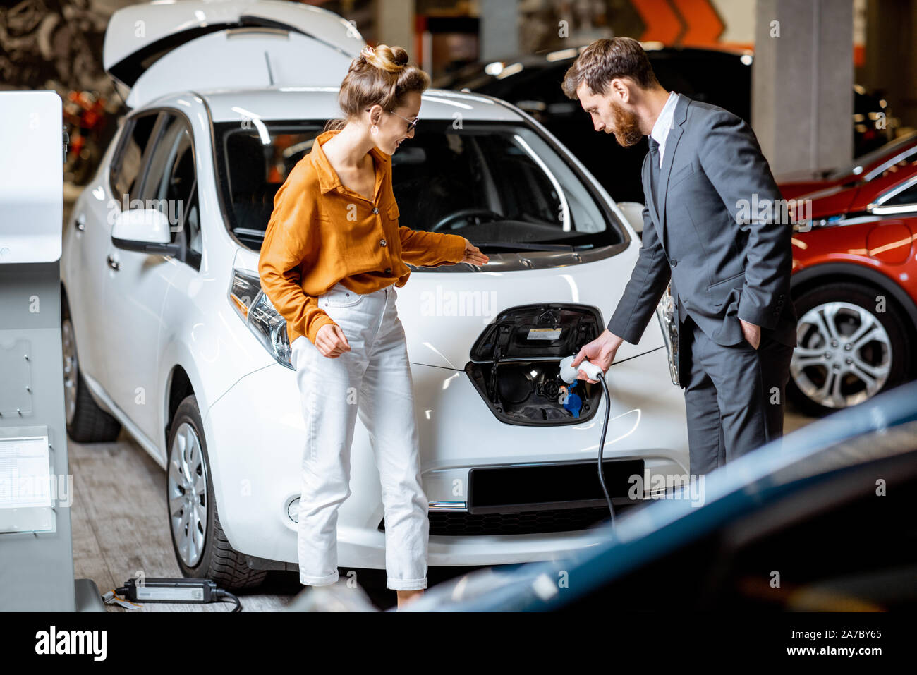 Sales Manager che mostra come caricare auto elettriche per un giovane client, collegando il filo nella presa auto presso la concessionaria auto Foto Stock