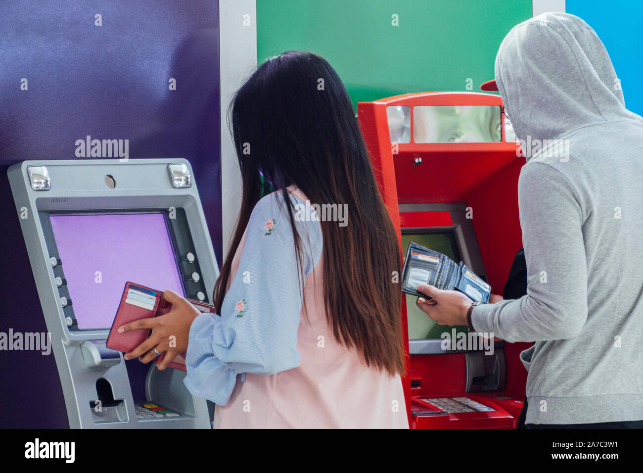 Giovani asiatici l uomo e la donna sono holding wallet e premendo il perno numero di protezione di ritirare denaro contante dalla carta di credito alla banca ATM macchina per il negozio Foto Stock
