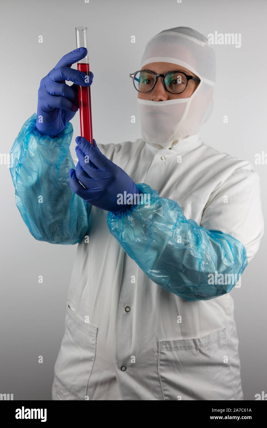 Giovane donna con occhiali, indossando il bianco, sterile, indumenti di protezione e guanti blu, tenendo un tubo con un campione liquido rosso per industria alimentare Foto Stock