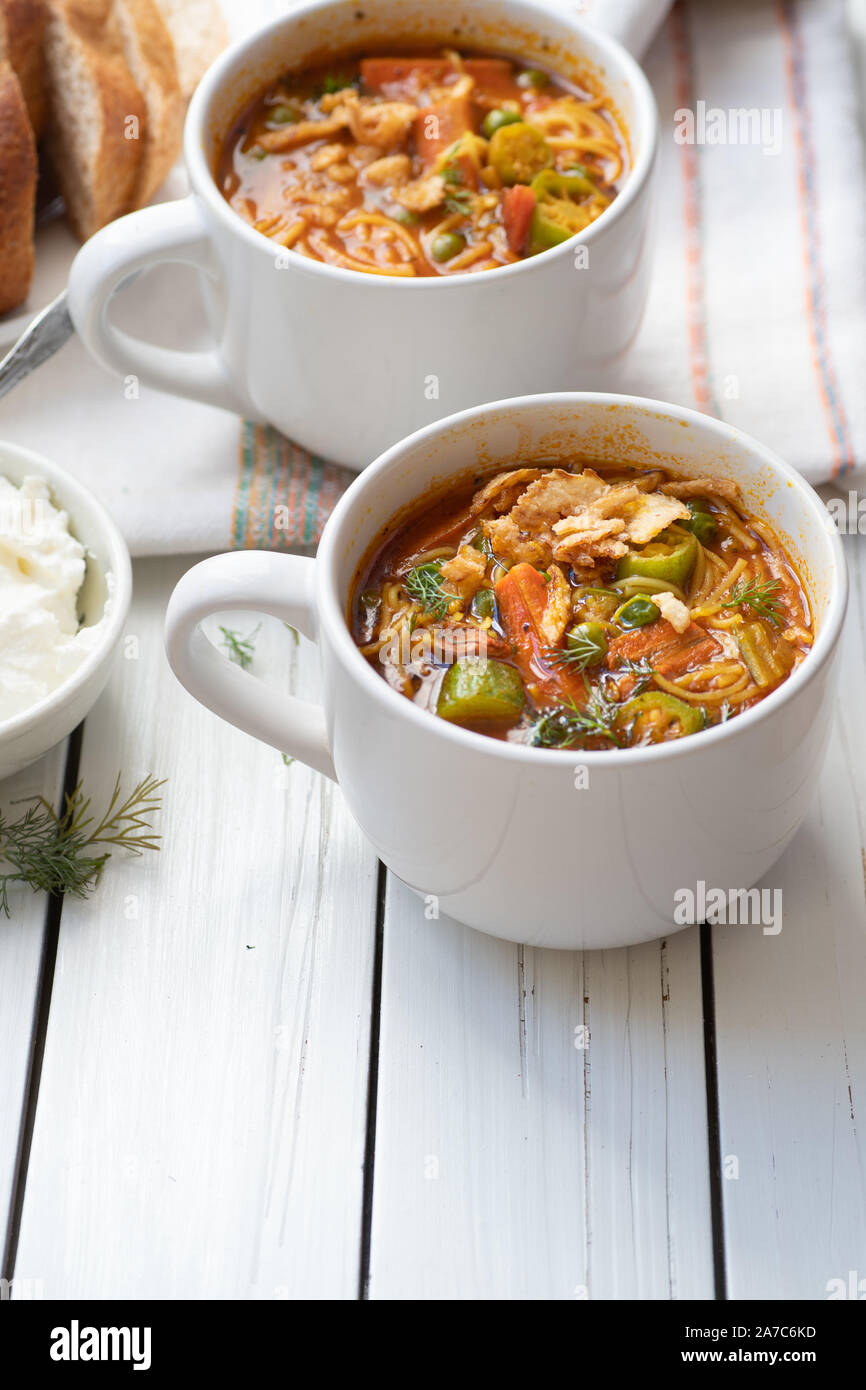 L'okra, piselli, carote e noodle soup servita in ceramica bianca tazze, bianco sul tavolo di legno Foto Stock