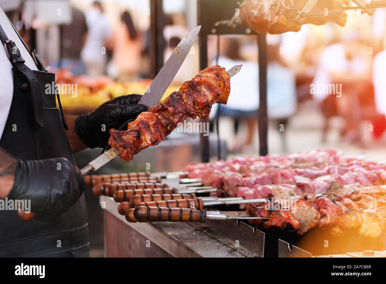 Chef per friggere la carne sulla griglia. Cuocere in nero grembiule fries carne sul fuoco. Barbecue all'aperto. Condizioni di luce solare intensa bokeh di fondo Foto Stock