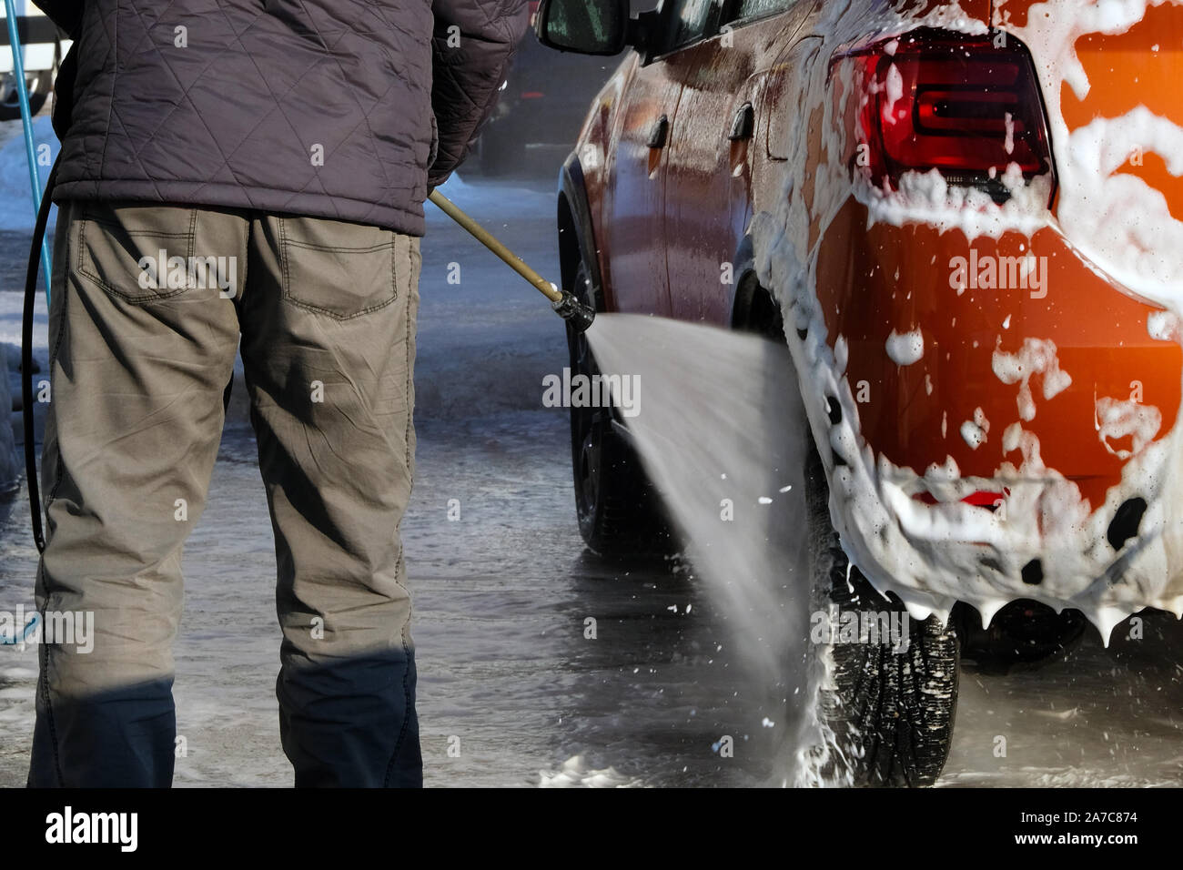L'uomo lava la sua vettura arancione a car wash. La pulizia con schiuma di sapone al self-service car wash. Acqua saponata scorre verso il basso. Foto Stock